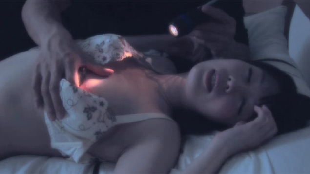 乳首をいじられながら、男性に懐中電灯で照らされる女性